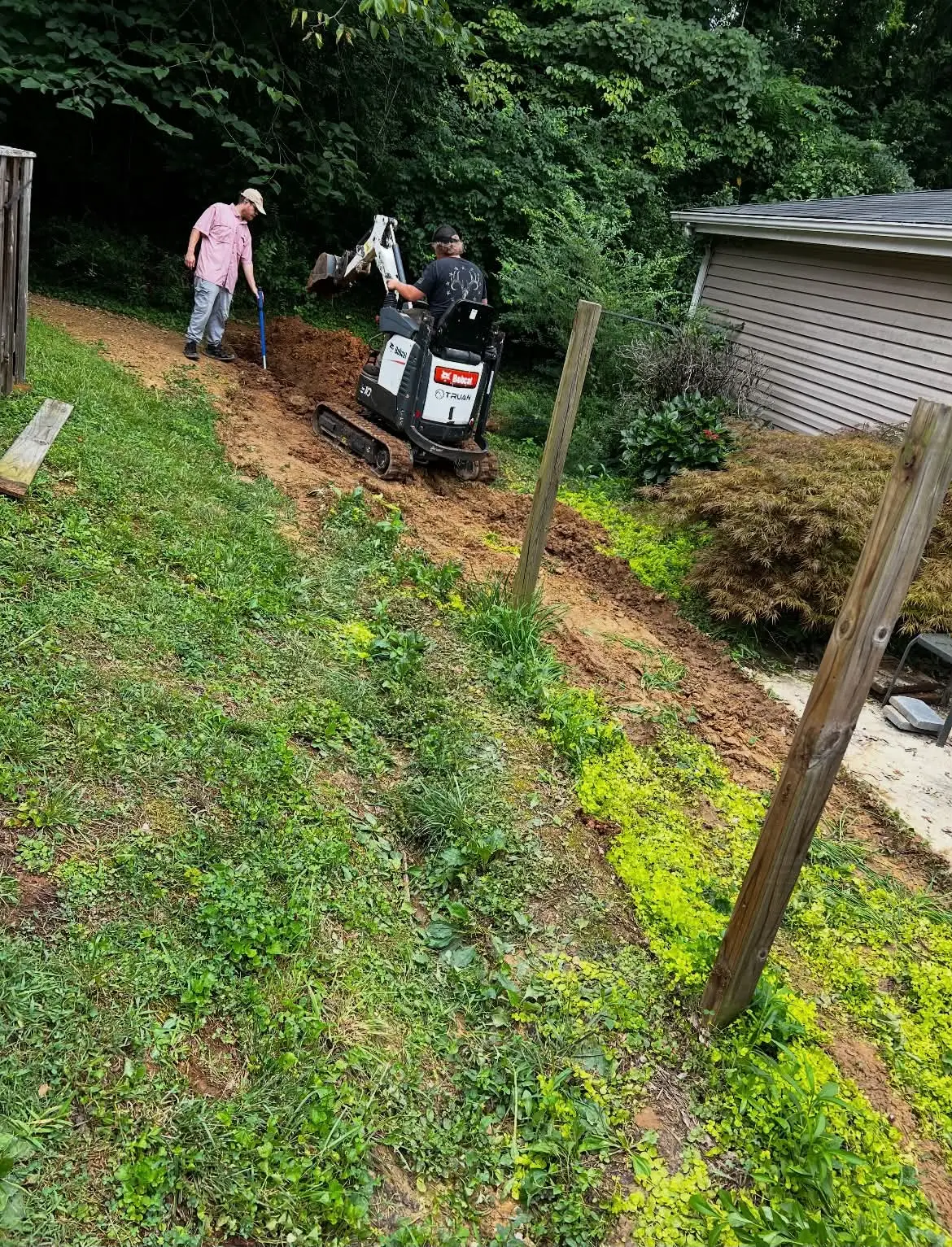 Mini excavator trenching along steep backyard slope for drainage work
