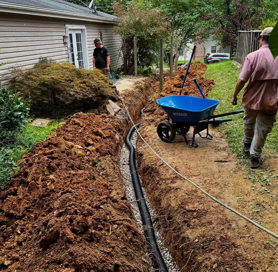 Drain pipe installed in gravel trench beside home during property restoration work